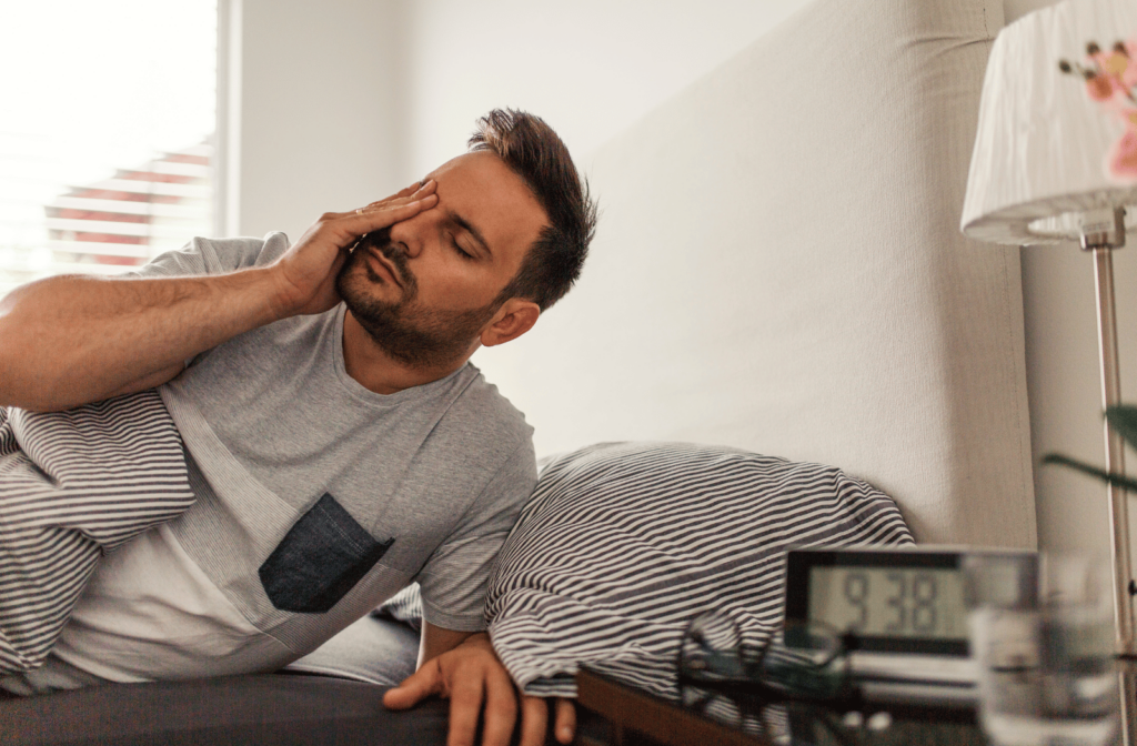 A man waking up in bed, rubbing his eyes as he gets up due to dry eye