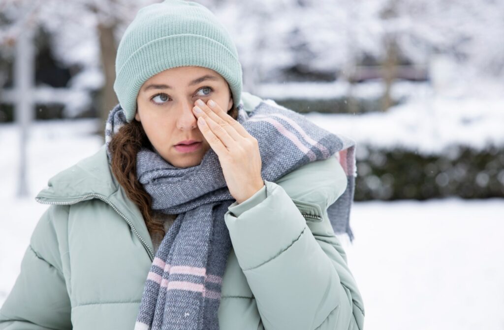 A woman rubbing her dry eyes while standing outside in the cold winter air