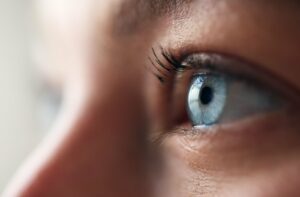 Macro close-up of a blue eye showing the reflective tear film on the surface of the cornea.