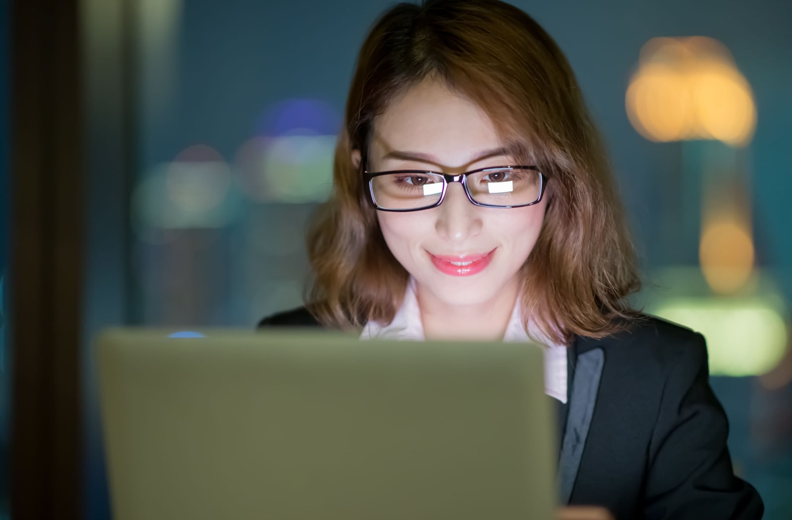 A woman wearing blue light glasses to protect her eyes while working in front of a computer screen.