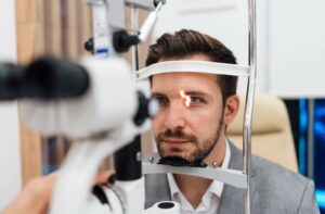 Patient sits at a slit lamp machine during an eye exam as a bright light is directed into his eye to check eye health.