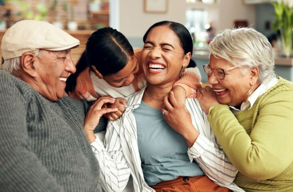 A joyful family sits together on a couch, laughing and hugging each other with big smiles.