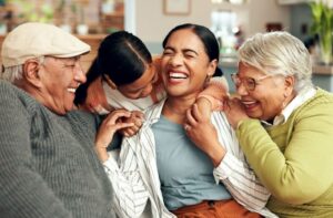 A joyful family sits together on a couch, laughing and hugging each other with big smiles.