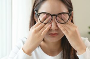 Woman rubbing eyes behind glasses, a common sign of dry eye symptoms.