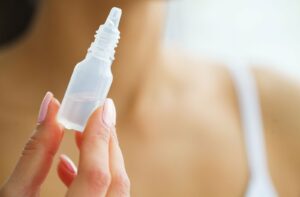 A close-up of a hand holding a small, clear dropper bottle containing eye drops.