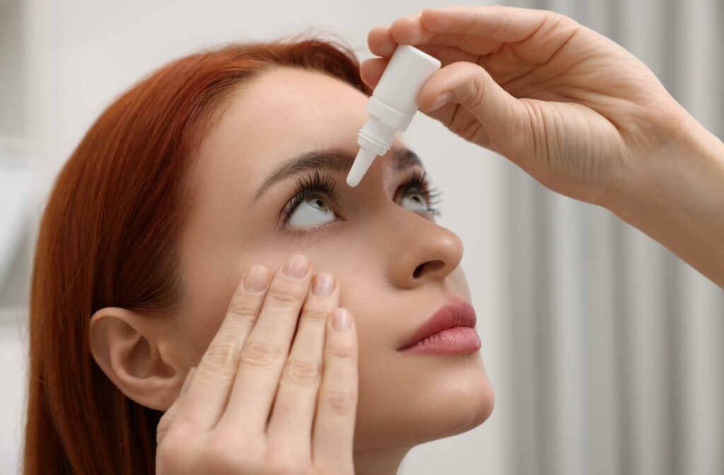 An individual looking upward while carefully administering eye drops into their eye from a white dropper bottle.